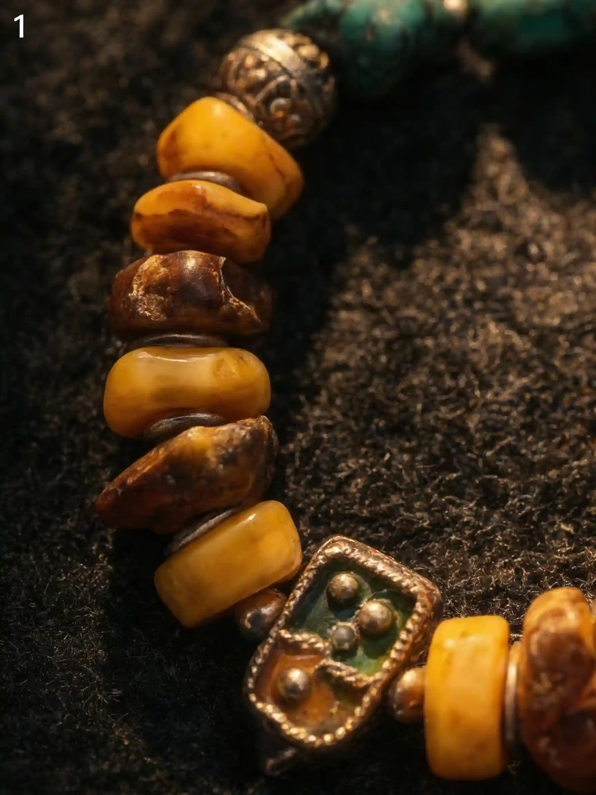 Detail of raw yellow amber beads and small green enamel spacer element