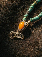 Detail of ornate metal hook clasp set with an oval amber cabochon and turquoise seed beads