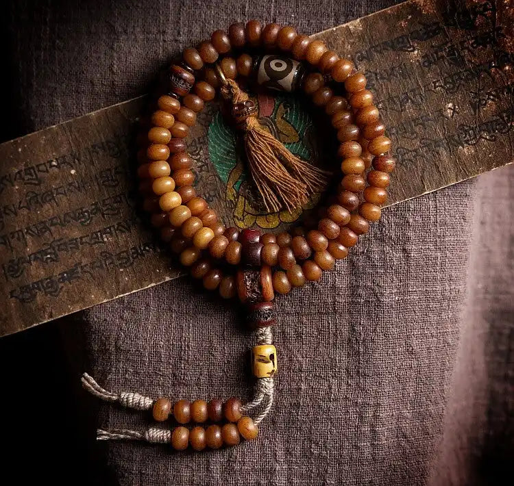 Coiled 108 natural yak bone prayer beads mala with Dzi bead and brown tassel on Tibetan manuscript